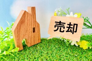 戸塚区の不動産売却をイメージした木製の家の模型と「売却」のプレート