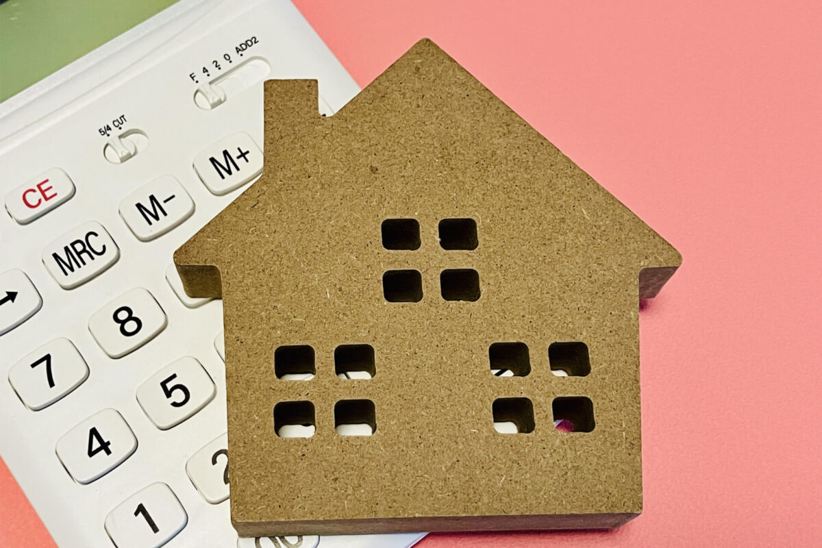 電卓と住宅模型｜不動産買取の査定価格や売却費用を検討するイメージ